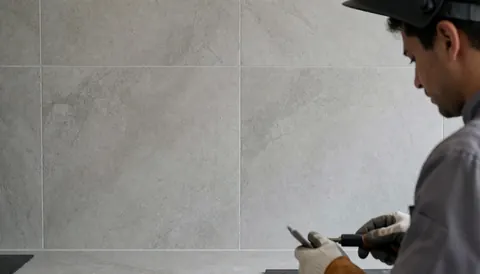 Installateur de cuisine travaillant sur un mur en porcelanate gris avec un outil à la main, scène professionnelle et propre.