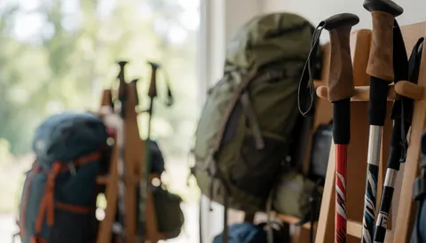 Bâtons de randonnée et sacs à dos posés sur des étagères en bois avec un fond flou et une lumière naturelle, idéal pour un refuge de montagne.