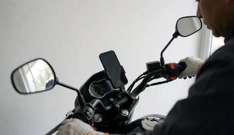 Moto-taxi équipé d'un téléphone dans un support, main gantée près du rétroviseur, fond blanc, idéal pour illustrer un service en action