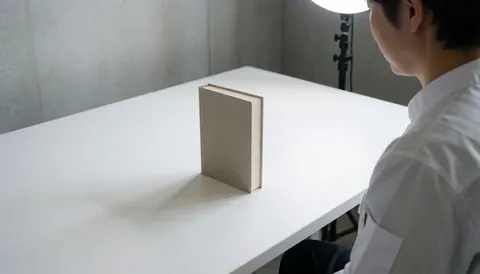 Photographe professionnel de produit en studio avec un livre à couverture rigide sur une table blanche et un mur en béton, éclairé par une lumière de studio.