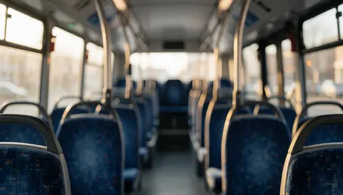 Intérieur d'un autobus avec des sièges bleus et des barres métalliques, éclairé par la lumière du coucher de soleil, idéal comme arrière-plan pour du texte.
