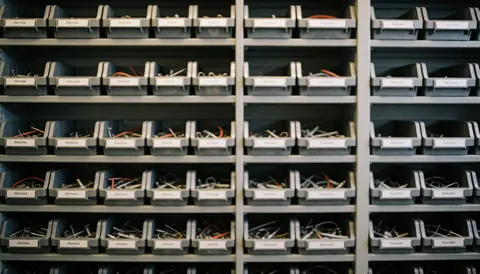 Étagère contenant des boîtes organisées de composants électroniques et câbles pour réparation de consoles, offrant un fond neutre et professionnel adapté à l'ajout de texte.