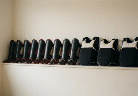 Protège-tibias et protège-poitrine rangés sur une étagère dans un dojo aux murs crème, idéal pour promouvoir un établissement d'arts martiaux.