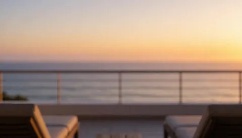 Terrasse avec chaises de plage et vue sur la mer au coucher du soleil, éclairée par une lumière dorée avec un dégradé d'orange et de violet, idéale pour ajouter du texte.