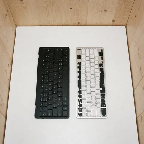 Un clavier noir complet et un clavier blanc sans touches posés sur une surface blanche, destinés à la réparation d'ordinateurs.
