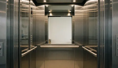 Vue intérieure d'un ascenseur moderne aux murs en acier inoxydable, avec barres métalliques et panneau de contrôle, adapté aux services de maintenance et réparation d'ascenseurs.