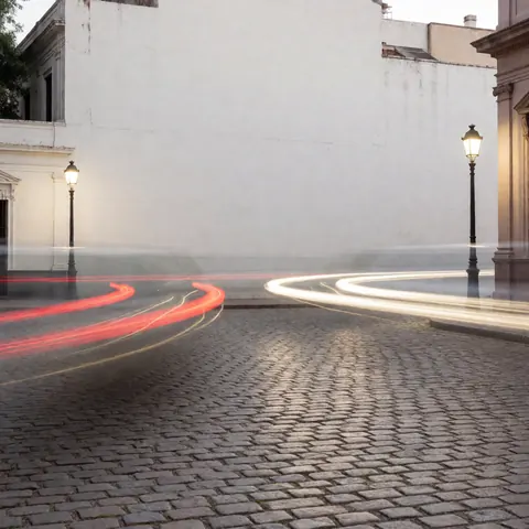 Place pavée nocturne avec traînées lumineuses de véhicules, éclairage public et bâtiments historiques, idéale pour un photographe cinétique