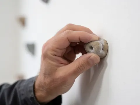 Gros plan d'une main adulte saisissant fermement une prise d'escalade sur un mur blanc, illustrant le détail d'une séance d'escalade en intérieur.