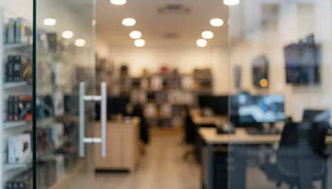 Arrière-plan d'un magasin de réparation d'ordinateurs avec des étagères de composants, des moniteurs et des lumières chaudes, idéal pour les textes commerciaux.