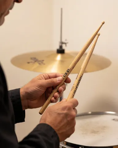 Mains d'un étudiant ajustant la prise des baguettes en bois devant une cymbale dans une académie de musique aux murs blancs.