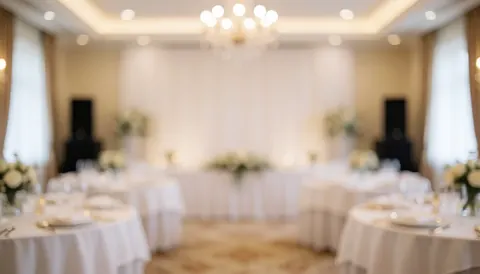 Fond de réception de mariage avec tables rondes couvertes de nappes blanches, arrangements floraux et lumières chaudes, idéal pour les services audio d'événements.