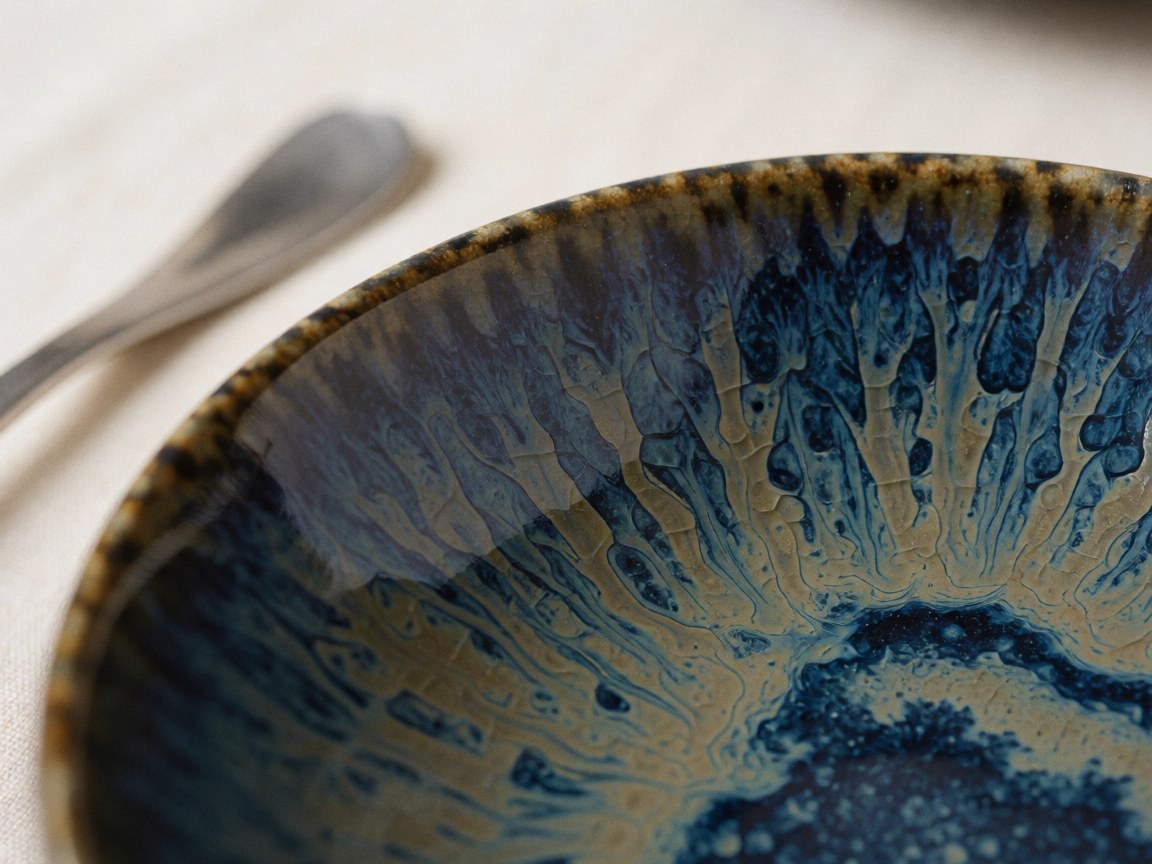 Détail d'un bol en céramique artisanale avec motif craquelé bleu et doré posé sur une nappe crème, idéal pour la décoration et la mise en scène de banquets.