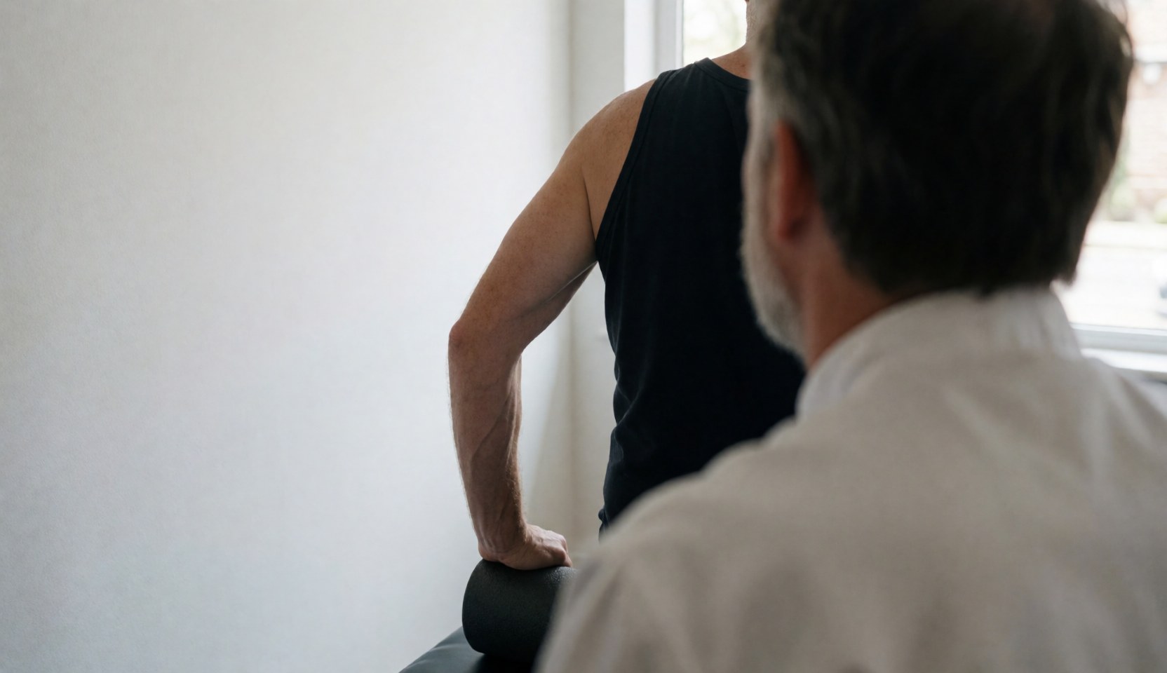 Une cliente utilise un rouleau de mousse pendant qu'un entraîneur l'assiste dans une salle aux murs blancs et à la lumière naturelle.