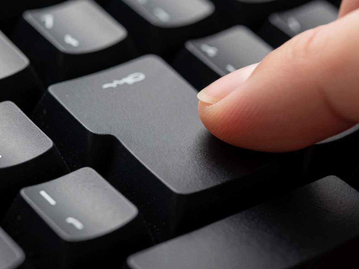 Gros plan d'un doigt humain en train d'appuyer sur une touche noire d'un clavier mécanique, mettant en valeur la texture et l'éclairage de studio.