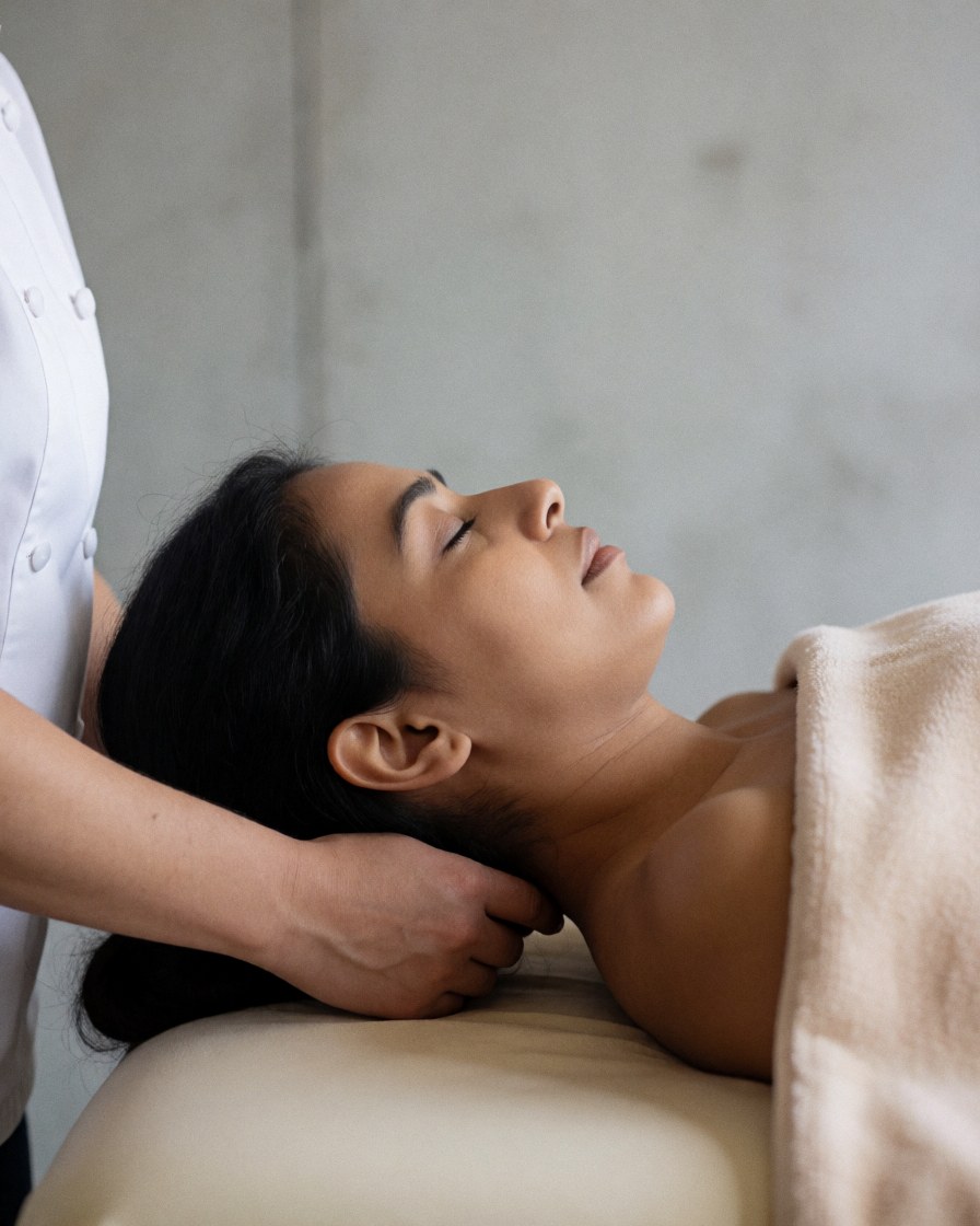 Un thérapeute effectue un massage cervical sur un client allongé sur une table de massage, entouré de serviettes douces et de murs en béton dans un environnement relaxant de spa.