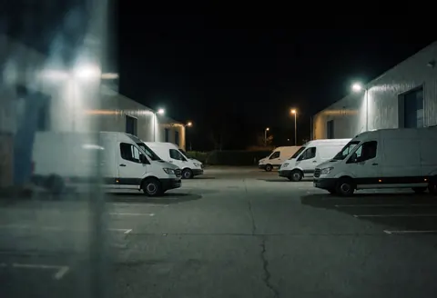 Des camions de fret stationnés dans un parc industriel nocturne, éclairage chaud, ambiance logistique et transport.