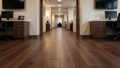 Couloir d'espace professionnel au sol en bois foncé, éclairage doux et mobilier de bureau, servant de fond neutre pour des textes promotionnels liés à l'installation de revêtements de sol.