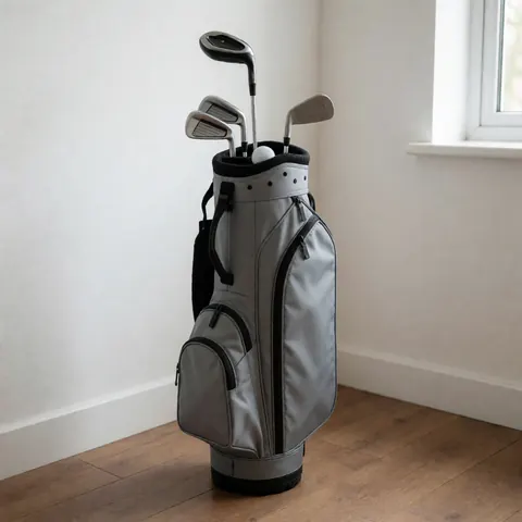 Sac de golf gris contenant des clubs et une balle posé sur un sol en bois devant un mur blanc, idéal pour un professionnel du golf.