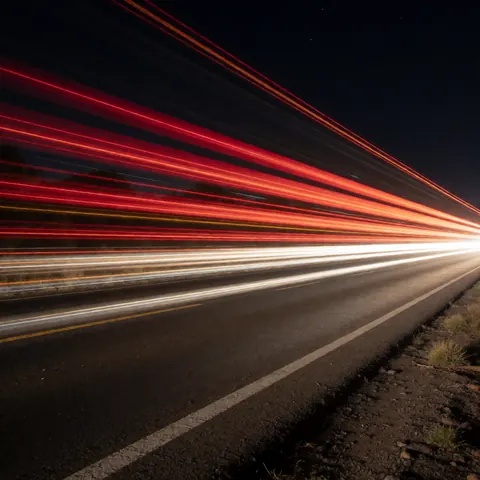 Photographie nocturne montrant des traînées lumineuses rouges et blanches de véhicules en mouvement sur une route, idéale pour un fonds textuel.