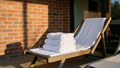 Transats en bois avec serviettes blanches sur une terrasse en briques, idéale pour une maison de vacances au bord de la piscine.