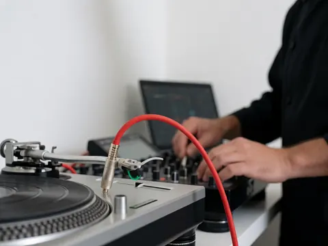 Câble rouge connecté à une platine vinyle et un mixeur, mains de DJ manipulant l'équipement professionnel sur une table blanche à fond blanc