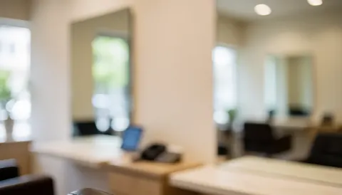 Arrière-plan de salon de beauté avec tables de travail, miroirs, éclairage encastré, murs beige et chaises, idéal pour textes commerciaux.