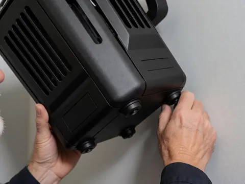 Des mains ajustent un projecteur professionnel noir avec ventilation sur un mur gris, utilisé pour l'éclairage d'événements.