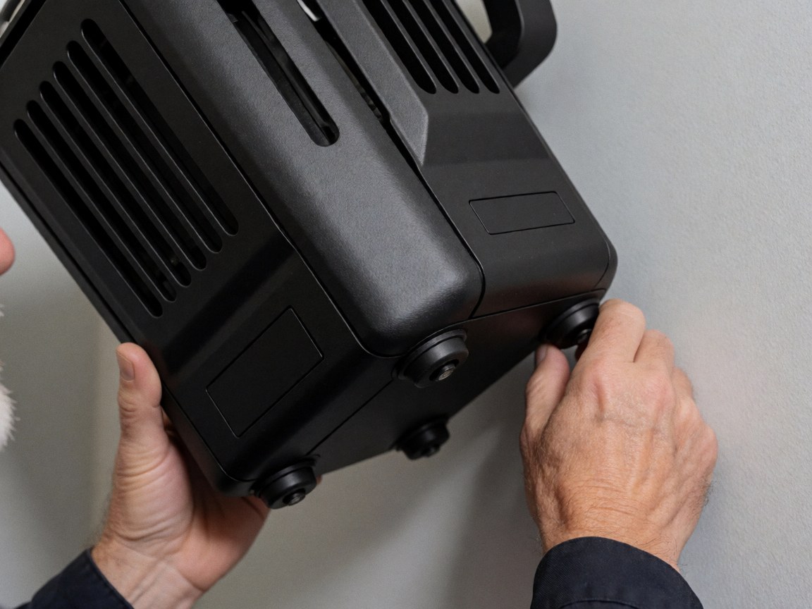 Des mains ajustent un projecteur professionnel noir avec ventilation sur un mur gris, utilisé pour l'éclairage d'événements.