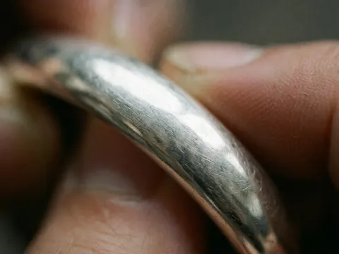 Gros plan d'un bracelet en argent avec texture et rayures visibles, tenu par des mains, pour des produits de thérapie naturelle.