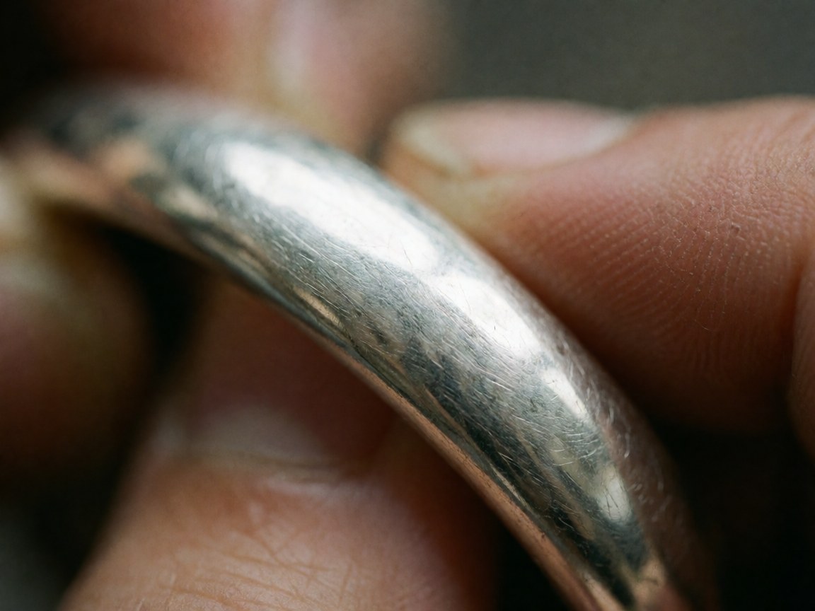 Gros plan d'un bracelet en argent avec texture et rayures visibles, tenu par des mains, pour des produits de thérapie naturelle.