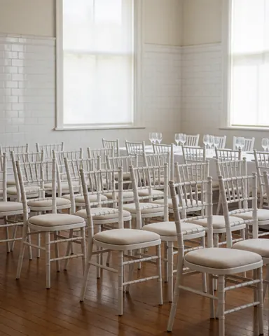 Chaises blanches Chiavari dans une salle d'événements avec murs carrelés et sol en bois, idéal pour les coordinateurs de fêtes.