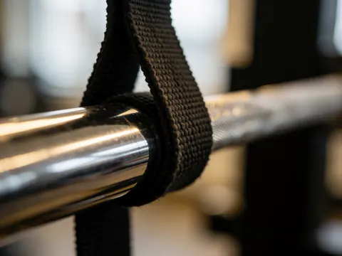 Bande noire d'entraînement attachée à une barre chromée dans un gymnase, avec des reflets métalliques et un flou d'arrière-plan.
