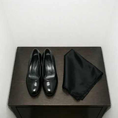 Paire de chaussures de danse de tango noires et un mouchoir en soie posés sur une table en bois sombre, évoquant l'univers du tango professionnel.