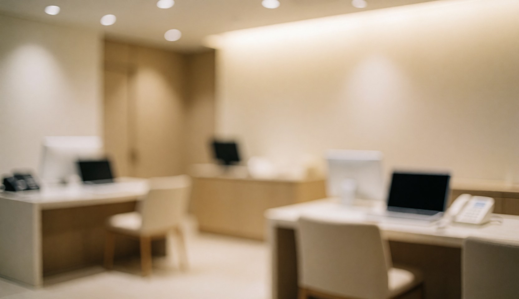 Arrière-plan flou d'une réception clinique moderne avec bureaux, ordinateurs et téléphones, éclairage chaleureux et meubles beige.