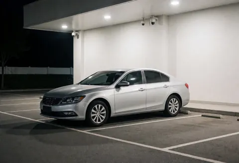 Un sedan argenté stationné dans un parking couvert éclairé, équipé de caméras de sécurité pour le transport nocturne.