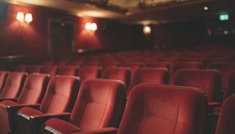Des sièges rouges en velours disposés dans un théâtre avec un éclairage chaleureux, servant de fond pour des textes sur des événements et la location d'espaces.