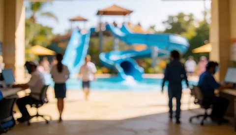 Arrière-plan flou de l'entrée d'un parc aquatique avec des personnes marchant et des toboggans bleus au loin, idéal pour ajouter du texte.