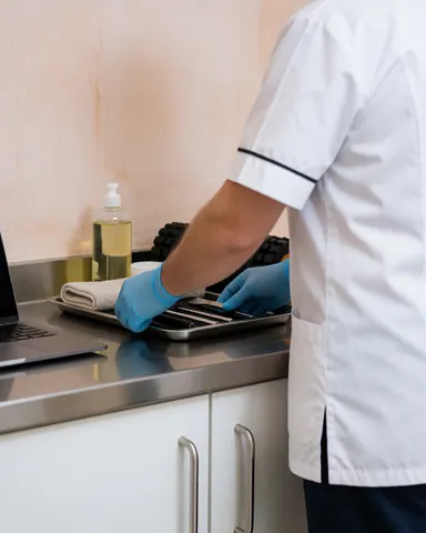 Un thérapeute portant des gants bleus range des outils sur un plateau métallique posé sur une table en acier inoxydable dans une clinique.
