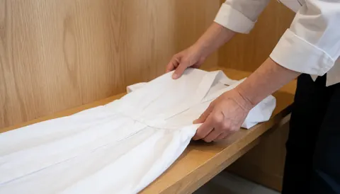 Des mains plient soigneusement une robe blanche sur une table en bois clair dans un cadre de bien-être.