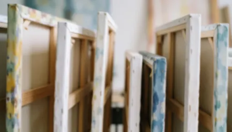 Plusieurs toiles avec des cadres peints disposées dans un atelier d'art, offrant un fond flou et une ambiance créative adaptée à l'ajout de texte.
