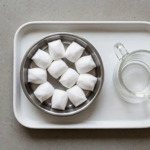 Des cotonettes humides placées dans un contenant en métal posé sur une assiette blanche, accompagnées d'un verre en verre, destinées à un massage avec ventouses.