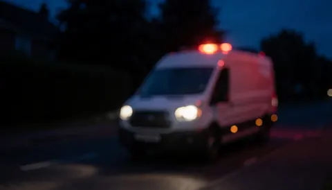 Arrière-plan flou d'une rue nocturne avec un camion blanc et des feux rouges d'urgence, idéal pour les services de réparation de chaudières.