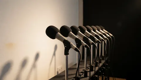 Microphones dynamiques montés sur des pieds métalliques, prêts pour des événements professionnels. Fond blanc et éclairage chaud créent une ambiance dramatique.