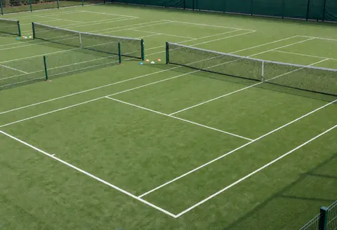 Trois courts de tennis avec surface synthétique verte, lignes blanches et filets, idéaux pour l'entraînement en extérieur.