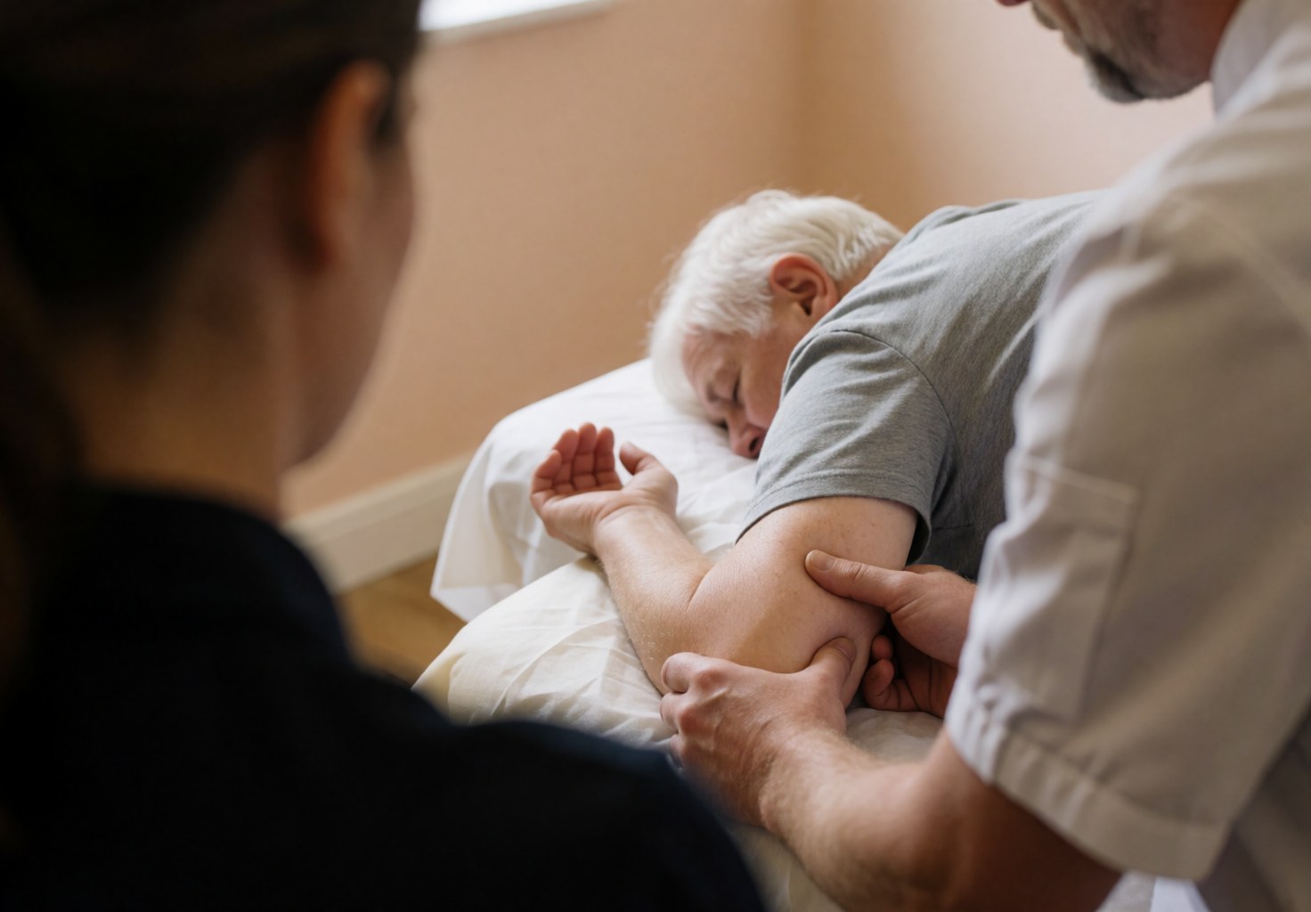 Un thérapeute réalise un massage sportif sur le bras d'un client âgé allongé sur une table de massage dans un cadre relaxant aux murs beige.