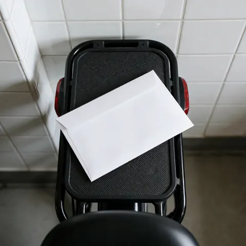 Un récipient blanc posé sur le porte-bagages d'un vélo urbain devant un mur de carreaux blancs éclairé par la lumière naturelle pour un service de livraison.