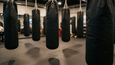 Fond de gymnastique avec plusieurs sacs de boxe noirs suspendus par des chaînes, sol en caoutchouc et éclairage chaud, idéal pour textes sur l'entraînement de boxe.