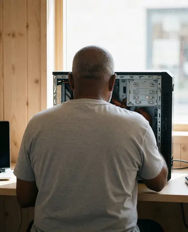 Technicien en train de réparer un ordinateur dans un bureau avec des murs en bois et une lumière naturelle provenant d'une fenêtre.