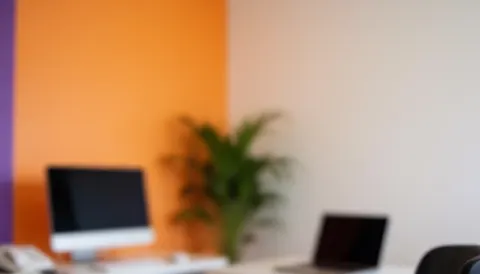 Espace de travail moderne avec murs orange et violet, ordinateur, ordinateur portable et plante, idéal pour superposer du texte.