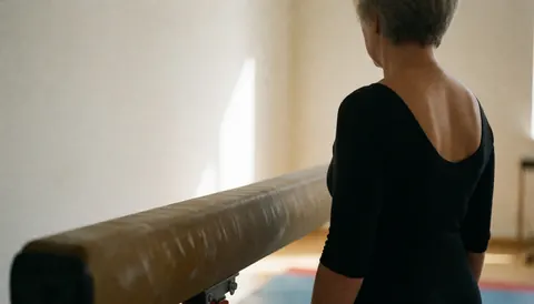 Entraîneur de gymnastique vu de dos à côté d'une poutre d'équilibre dans un gymnase aux murs blancs et à la lumière naturelle, idéal pour une page d'accueil de site web